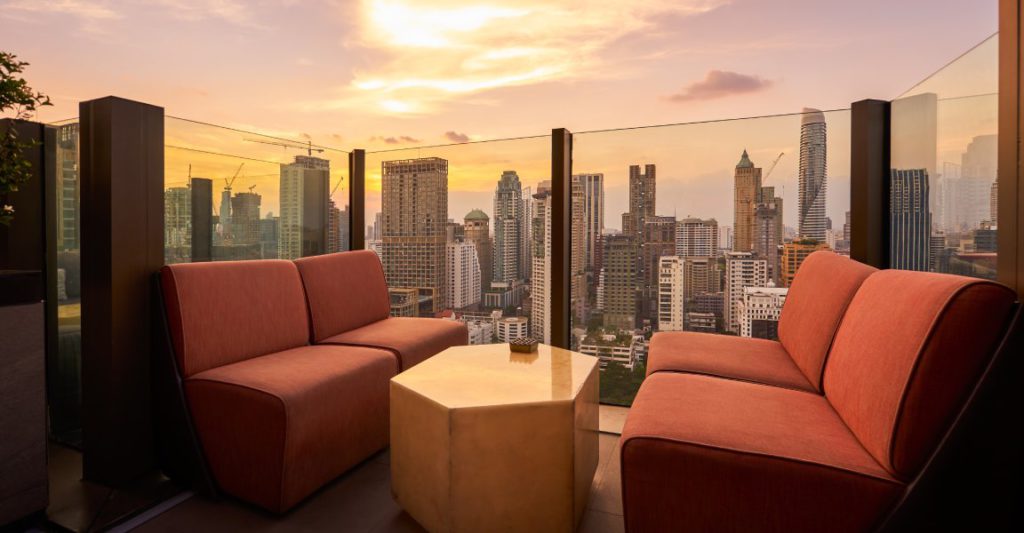 Comfortable sofa unit and hexagon table on a rooftop bar next to a glass fence overlooking a big city