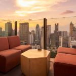 Comfortable sofa unit and hexagon table on a rooftop bar next to a glass fence overlooking a big city