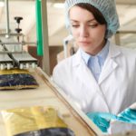 A worker at a food processing plant inspects sealed bags as they climb up a conveyor belt.