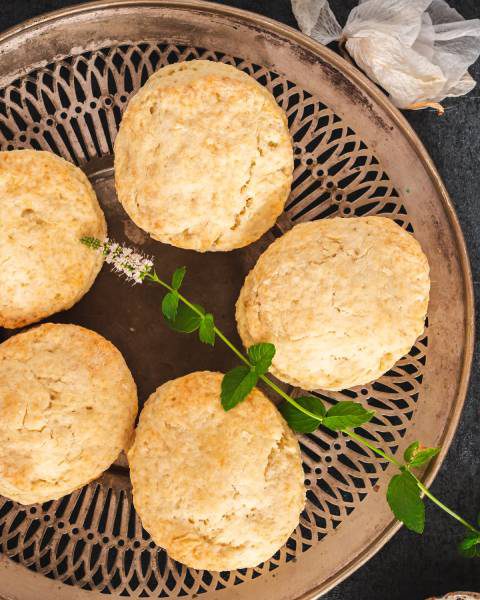 Six southern-style biscuits adorned with green garnishes are neatly arranged on a circular wooden tray.