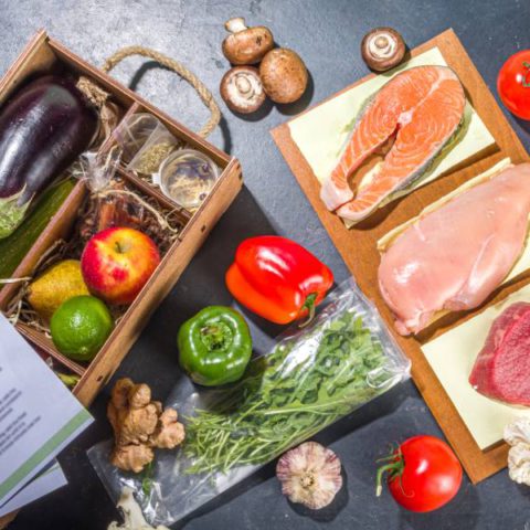 The ingredients of a meal delivery kit displayed on a black surface. Some recipe papers are lying on top of the box.