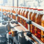 A conveyor belt in a beverage manufacturing facility with glass bottles containing juice. Custom filtration improved quality.